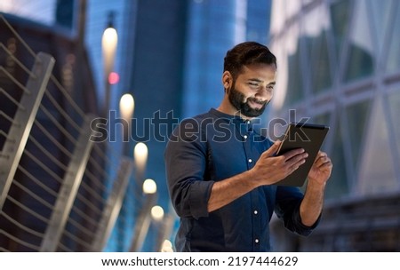 Rich successful eastern indian business man professional entrepreneur standing outdoors on street holding using digital tablet online technology in night big city with urban lights and skyscrapers. Royalty-Free Stock Photo #2197444629