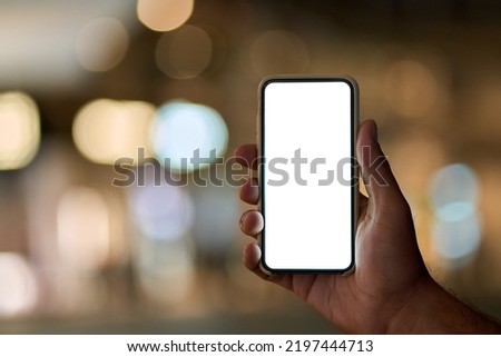 Male hand holding smartphone with white mock up screen on night city lights background. Man showing blank mobile display mockup template of cell phone with empty space for apps advertising concept
