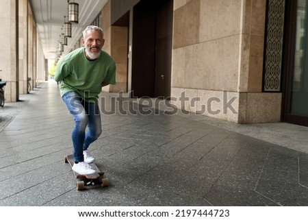 Active energetic happy cool gray haired old adult man skateboarding on city street, smiling sporty fit middle aged mature older male professional skater having fun enjoying riding skateboard outdoor. Royalty-Free Stock Photo #2197444723