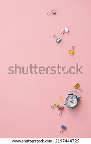 Small alarm clock, fasteners on pink background, flat lay top view. Teaching time urgent ring for children education start. Back to school, get ready for learning concept. Vertical. Copy space