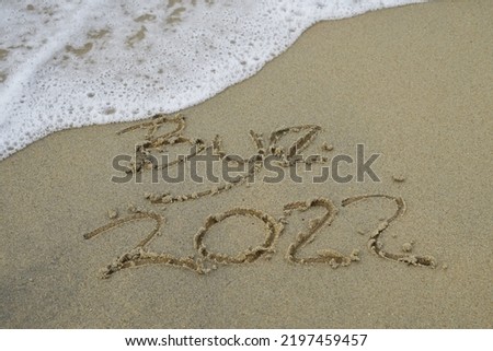 Bye 2022 text message handwritten on sand background. Holiday postcard template.