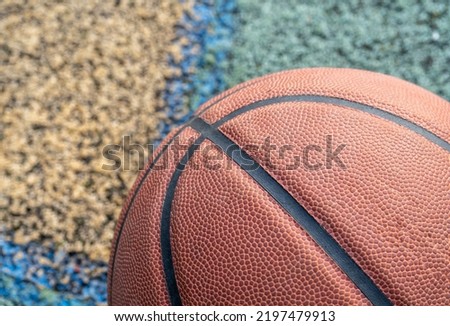 Orange basketball ball on the ground. Close-up ball on the red court. Basketball on the street or indoor court. Sports gear without people. Minimalism. Template, sport background