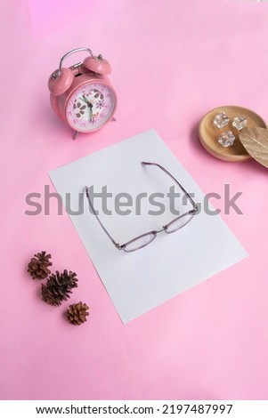 Round glasses in the photo from above with minimalist concept on purple paper background with alarm clock decoration, dry leaves and fir tree flowers
