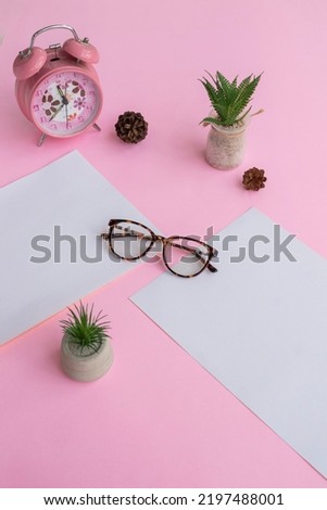 Cat's eye glasses in the photo from above with a minimalist concept on a purple paper background with an alarm clock decoration and dry leaves
