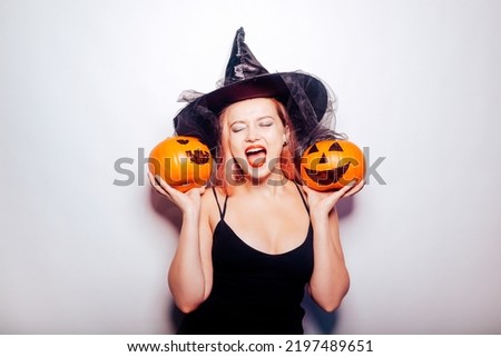 Beautiful girl witch is holding a pumpkin in her hands. Woman celebrating halloween, joy and a smile on her face. Autumn holidays and parties