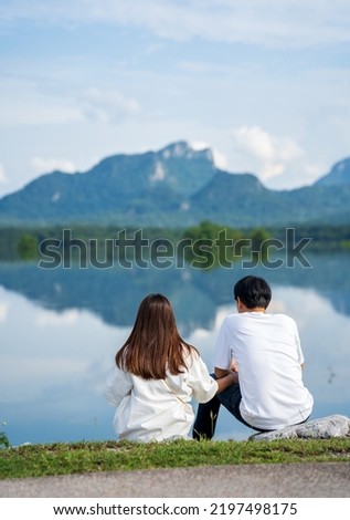two young people sitting on a lake with mountains background and admire the beauty of nature