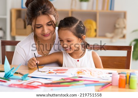 Young mother looking how her daughter drawing a picture