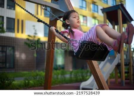 Girl on swing. Child on playground. Asian preschool girl. Rope swing in yard of house. Girl in pink dress rests in summer.