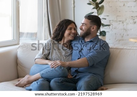 Beautiful millennial couple in love sit on sofa enjoy weekend at modern home, talking, feel happy. Latina wife, Caucasian husband spend free time relax in living room. Dating, homeowner family concept Royalty-Free Stock Photo #2197528969