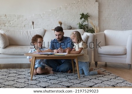 Loving father his diverse pre-schoolers children drawing pictures with colored pencils in sketchbook sit at table at home. Family weekend leisure, creative hobby and pastime, care and custody concept