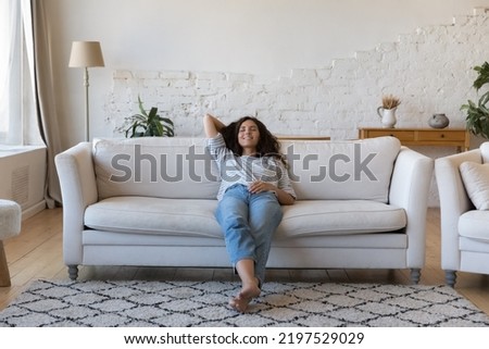 Latina woman daydream relax on sofa at home, housewife accomplish household chores reduces exhaustion, rest alone in living room, full-length. Air condition system inside, stress-free weekend concept Royalty-Free Stock Photo #2197529029