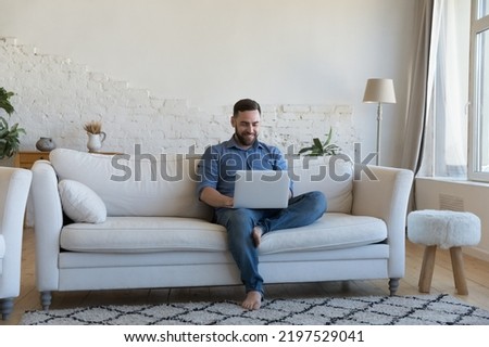 Man spend day off at home using modern laptop, smile enjoy pleasant chat in social media, buying goods, make easy comfort order seated on sofa with wireless computer. Tech, business, freelance concept Royalty-Free Stock Photo #2197529041