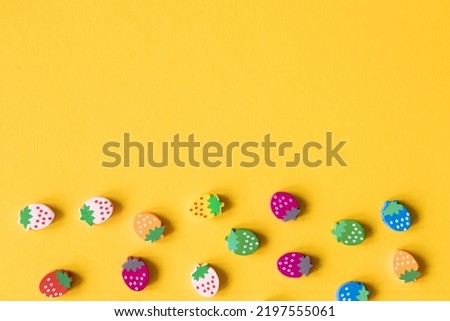 Colored wooden figures in the form of strawberries on a yellow background