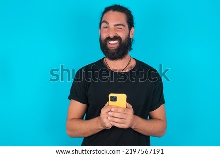 young bearded man wearing black T-shirt over blue studio background taking a selfie  celebrating success