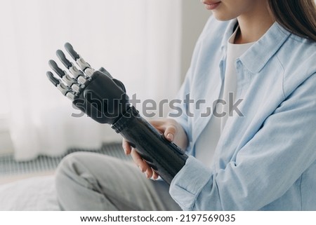 Women with disability customizing her sensory prosthetic arm, close-up. Female with disability using robotic prosthesis after limb loss. Application of bionic hands. Medical technologies. Royalty-Free Stock Photo #2197569035