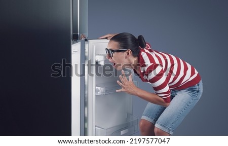 Shocked disappointed woman looking in the empty fridge at home