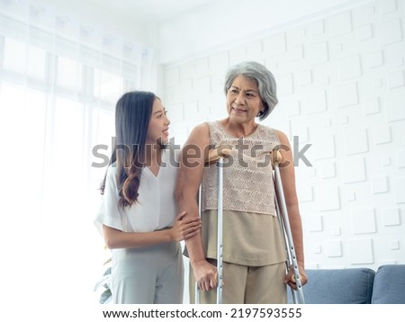 Elderly woman trying to walk on crutches standing held and supported in arms by young Asian female carefully in recovery room, helping old women, health care, senior therapy patient at home concept. Royalty-Free Stock Photo #2197593555