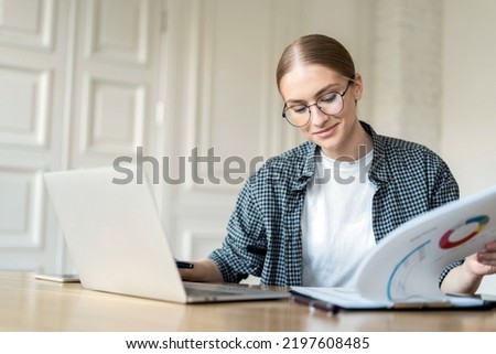 A woman with glasses uses a laptop, works in a new office, uses online training documents