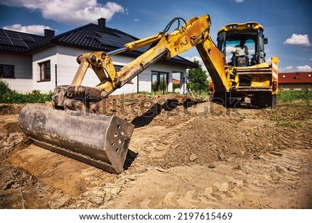 Excavator working at house construction site - digging foundations for modern house. Beginning of house building. Earth moving and foundation preparation. Royalty-Free Stock Photo #2197615469