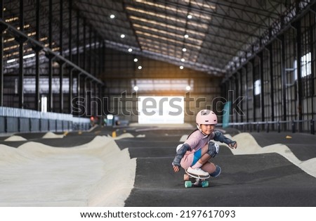 asian child skater or kid girl fun playing skateboard or ride surf skate in indoor pump track in skate park by extreme sports to wearing helmet elbow pads wrist knee support for body safety on summer Royalty-Free Stock Photo #2197617093