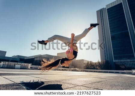 Young sportswoman performing a front flip outdoors in city. Female athlete practicing tricking against an urban background. Royalty-Free Stock Photo #2197627523