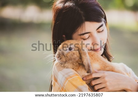 beautiful pretty portrait of young Asian woman person with cute rabbit in pet and animal care concept, happy female holding bunny at nature outdoor field with friendship, easter concept