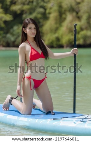 Young woman wearing red bikini standing on knees on paddle board for sup surfing in the sea on sunny day,holliday summer vacation concept