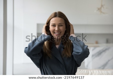 Cheerful beautiful 30s Caucasian woman home head shot portrait. Pretty lady in casual trendy overcoat, trench, coat looking at camera with toothy smile, laughing, adjusting long hair. Fashion