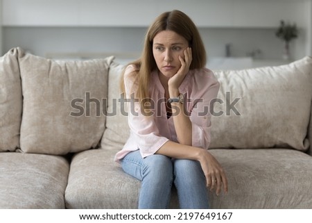 Tired bored woman suffering from apathy, boredom, laziness, procrastination, sitting on coach at home, leaning head on hand, looking away. Frustrated lady feeling depressed, thinking over problems Royalty-Free Stock Photo #2197649167