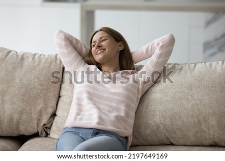 Cheerful pretty lazy 30s woman sitting on comfortable home sofa, leaning on back, looking away, enjoying relaxation, leisure, comfort, dreaming, thinking, smiling at breathing fresh air Royalty-Free Stock Photo #2197649169