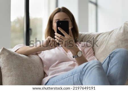 Young millennial unrecognizable smartphone user woman resting on home sofa, holding mobile phone, using online app, shopping on Internet, chatting. Communication