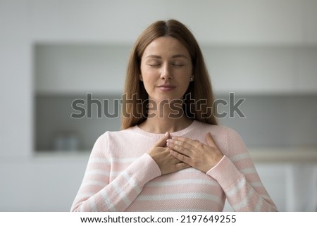 Peaceful beautiful Caucasian woman touching chest with both stacked hands. Grateful female model expressing gratitude, love, recognition. Pray, religion, faith Royalty-Free Stock Photo #2197649255