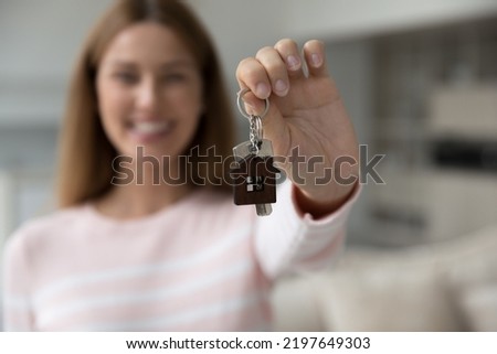 Happy house buyer woman holding keys at camera. Hand close up with female model in blurred background. Real estate agent, seller, mortgage broker offering apartment for rent, buying