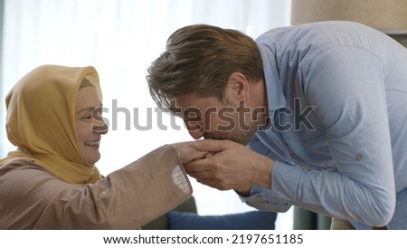 Young man kisses his mother's hand during Eid Mubarak (Turkish Ramadan or Şeker Bayram).The man kisses her hand to show respect to her veiled mother.Muslim holiday traditions concept. Royalty-Free Stock Photo #2197651185