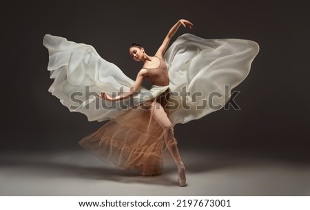 Ballerina. Young graceful woman ballet dancer, dressed in professional outfit, shoes and beige skirt with white flying fabric wings.Girl is demonstrating dancing skill. Beauty of classic ballet dance