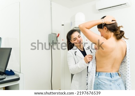 Smiling female doctor helping a young woman putting on a robe before doing a mammogram x-ray to check for breast cancer at the hospital 