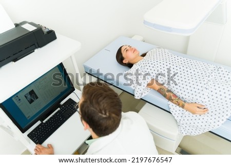 Top view of a sick female patient and radiologist technician doing a densitometry medical exam at the imaging diagnostic center