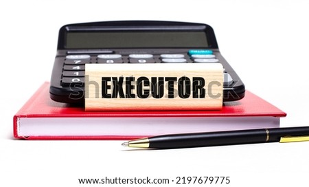 A burgundy notebook on a white background. On it is a black calculator, a pen and a wooden block with a EXECUTOR text. Business concept