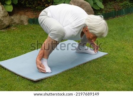 an age-old gray-haired woman does therapeutic exercises to stretch the muscles of the back, spine. High quality photo