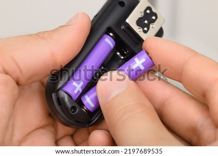 Hands replacing purple AAA alkaline battery in the black electronic device. Royalty-Free Stock Photo #2197689535