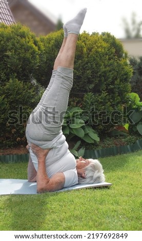 An elderly athletic woman does a candlestick exercise on the grass in the park. High quality photo