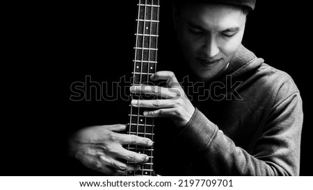 black and white portrait of smiling asian professional musician posing on bass guitar, isolated on black Royalty-Free Stock Photo #2197709701