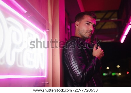 Serious man stands next to a neon sign "open" on the night city street.