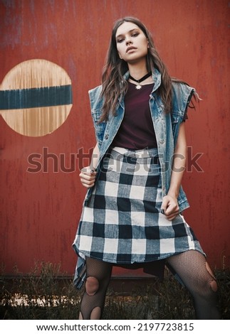 Outdoor portrait of the pretty grunge (rock) girl standing at the wall. Informal model dressed in jean jacket, checkered shirt and holey tights Royalty-Free Stock Photo #2197723815