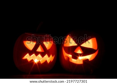 Two Halloween pumpkins with burning candles inside on black background