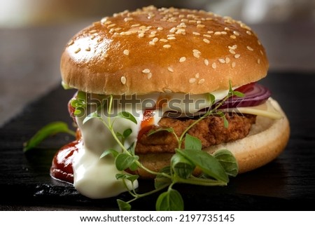 Close up of a cheeseburger with tomato and mayonnaise sauce on slate with green oregano