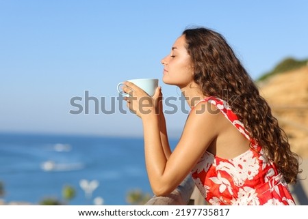 Side view portrait of a woman in red dress relaxing smelling coffee on the beach Royalty-Free Stock Photo #2197735817