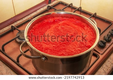 A woman prepares fresh healthy juice from tomatoes. Freshly made tomato juice is boiled in a saucepan and preserved for long-term storage. Diet concept for a healthy lifestyle. Royalty-Free Stock Photo #2197742913