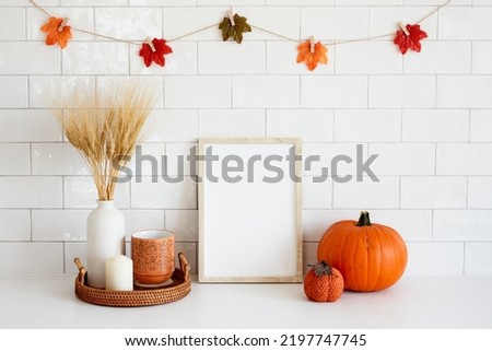 Frame mockup in cozy fall home interior with Halloween decor, pumpkins, vase of dried wheat, candle, coffee cup. Autumn mood, Halloween or Thanksgiving concept.