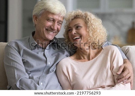 Happy cheerful elder senior couple in love relaxing on comfortable home sofa, hugging with care, gratitude, affection, talking, chatting, laughing, enjoying leisure time, relationship, dating Royalty-Free Stock Photo #2197756293